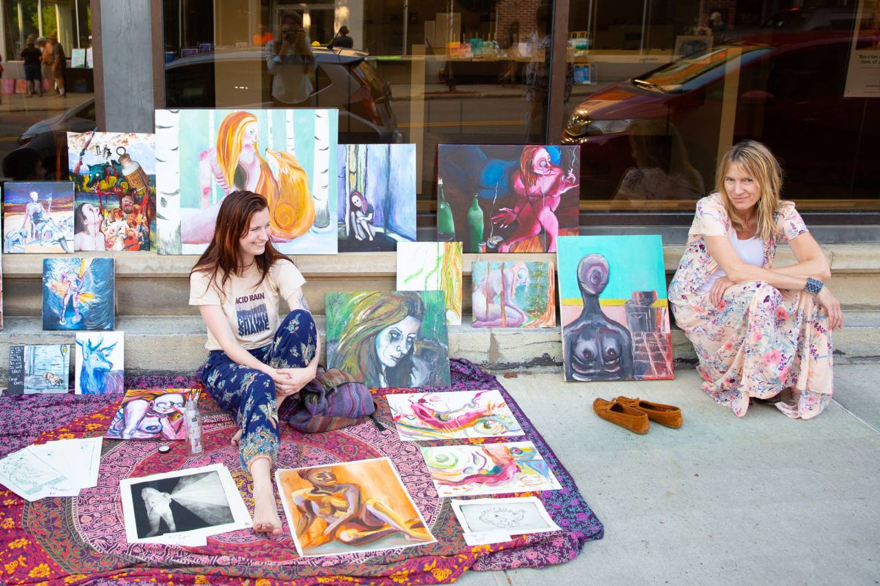Two women showcase their art on the sidewalk.