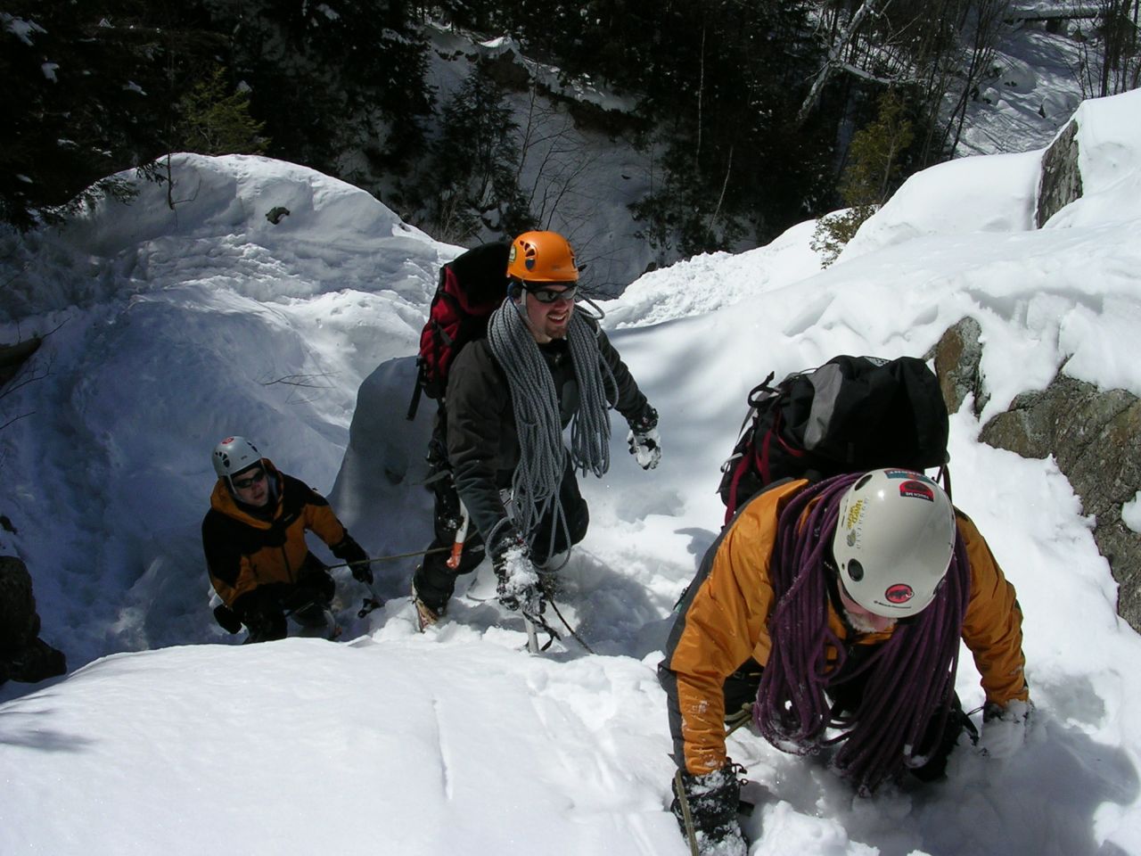 Three men climb to the top of a mountain in winter.