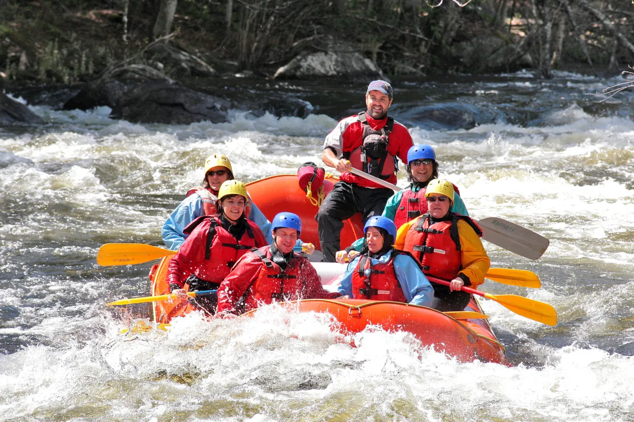 A group of people paddle in a raft on white water in a river.