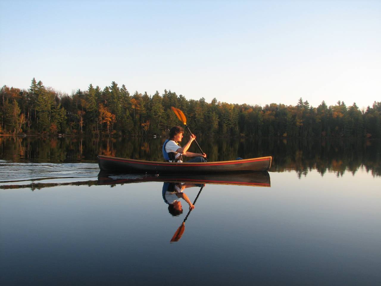 A person canoeing on a glassy lake during fall.