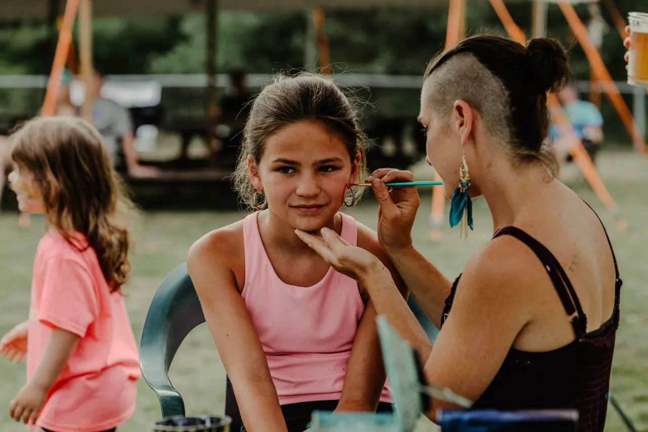 A young girl gets her face painted by a woman. 