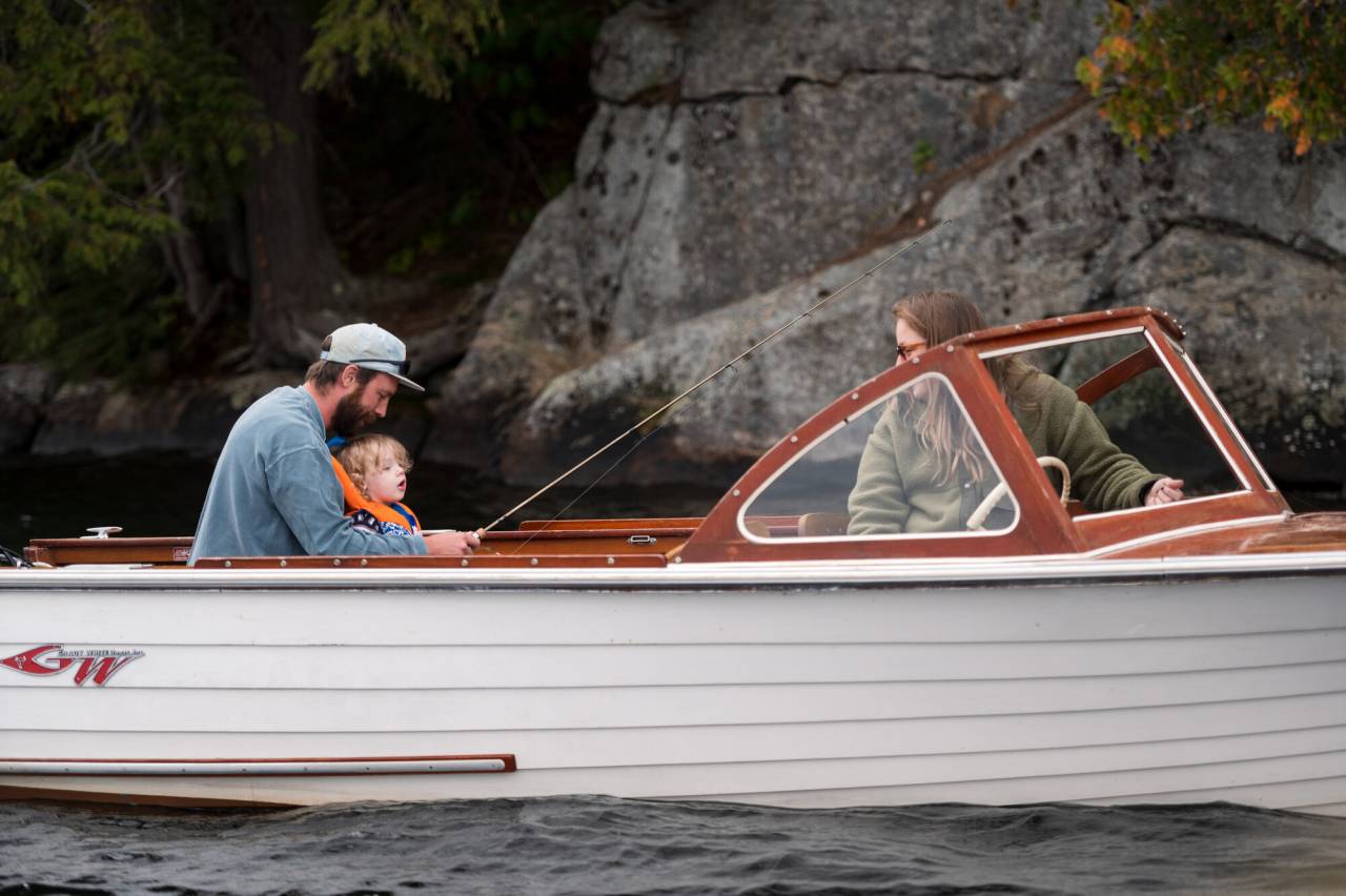 A man fishes with his family from a white boat. 