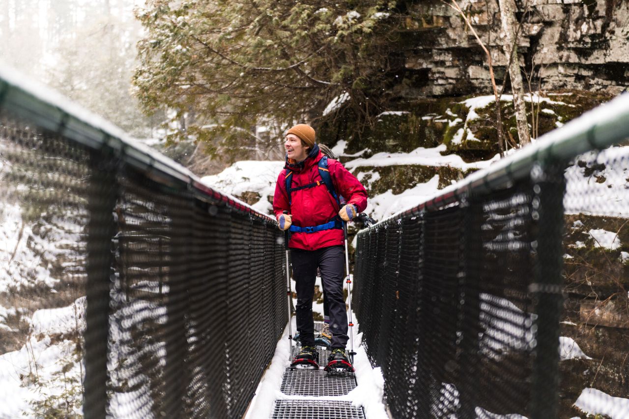A person snowshoeing over a bridge.