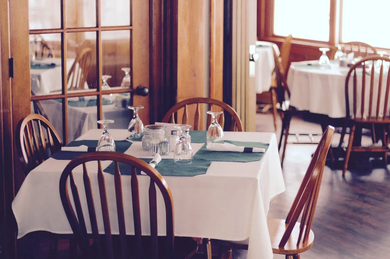 A square dining table with a white tablecloth and china at a naturally-lit restaurant dining room.