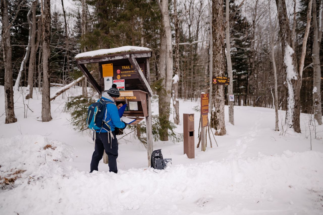 A man in a blue jacket signs into a trail in winter. 