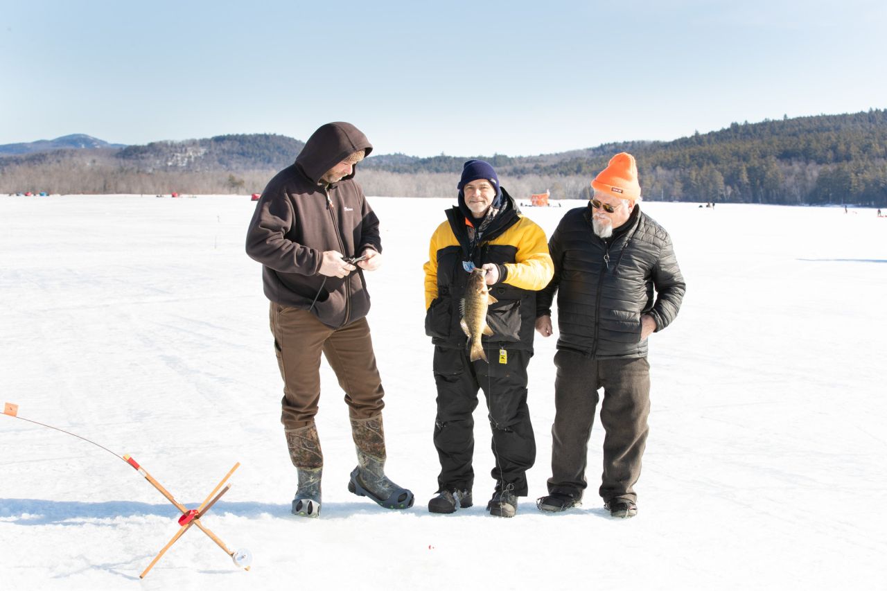 Three men smile and pose with a fish caught from ice fishing.