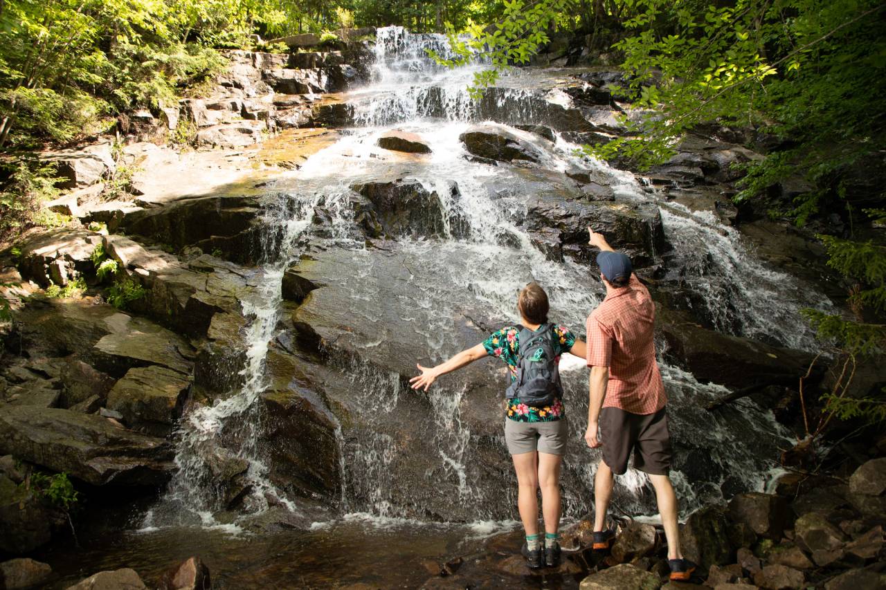 A man and woman stand in front of a flowing waterfall.