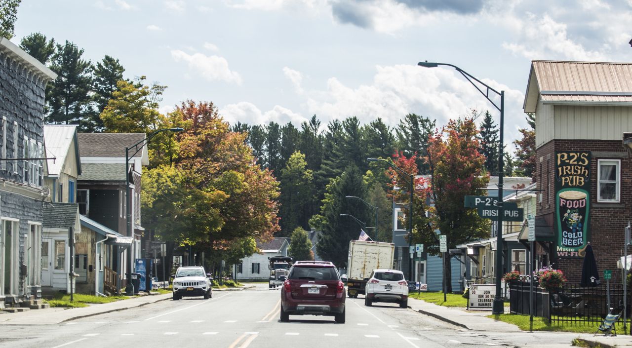 A car drives down a downtown road surrounded by trees and neighborhoods in fall. 