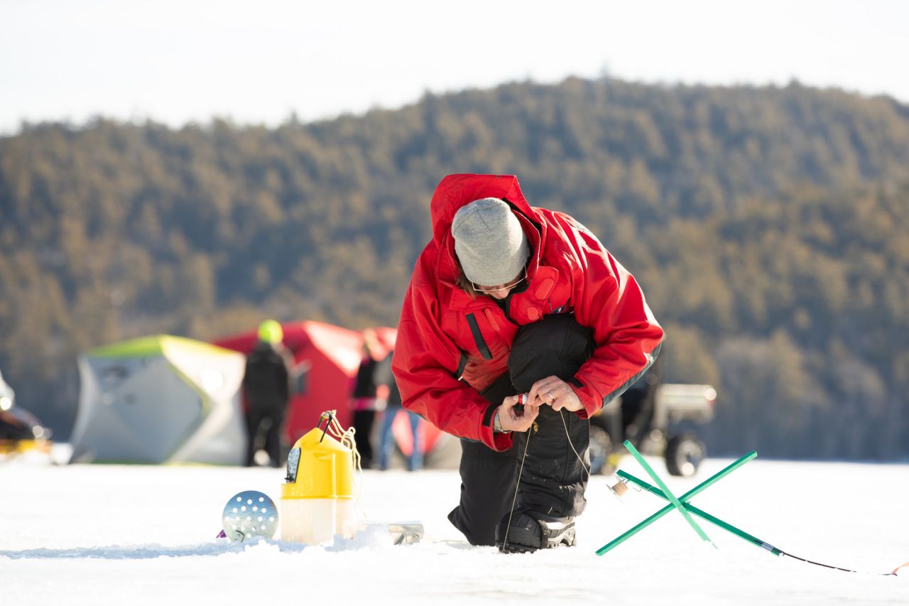 A man in a red jacket sets up a line ice fishing. 