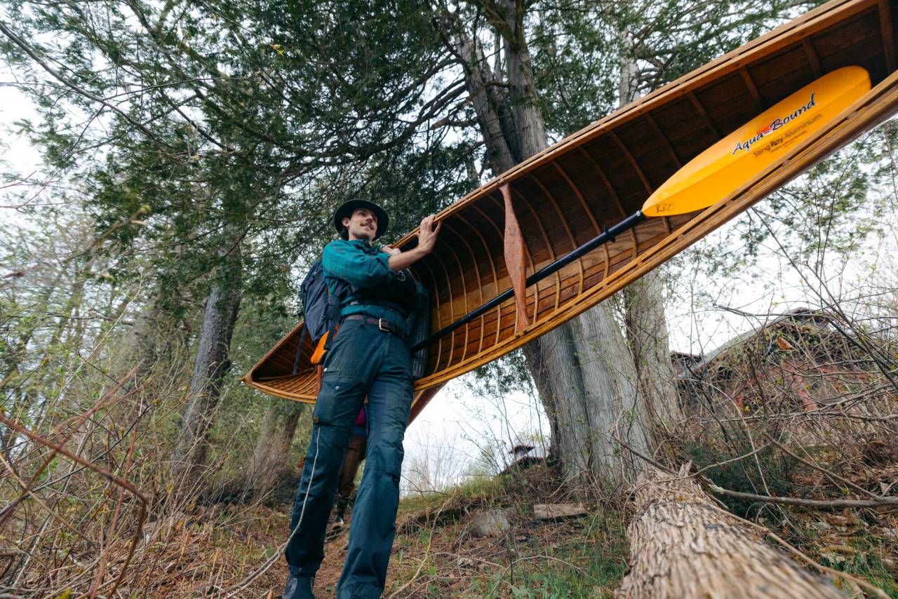 A man walks with a canoe on his shoulder. 