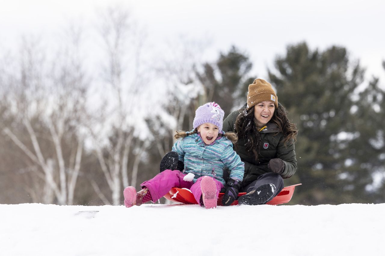 A woman and her young daughter sled down a hill in winter. 