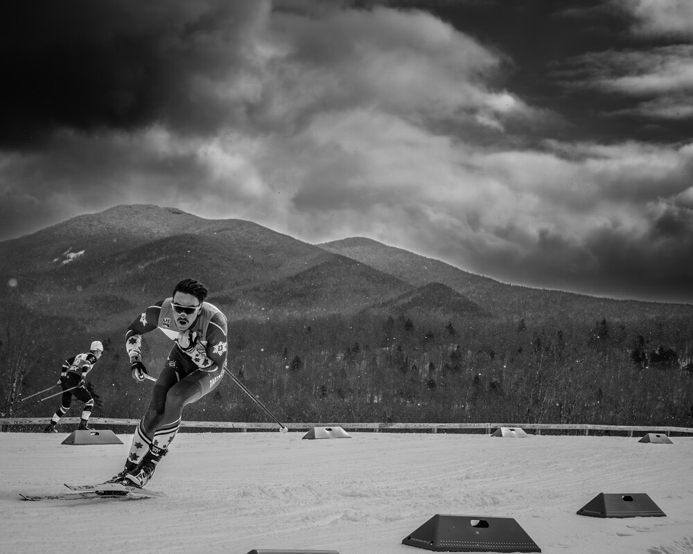 Black and white photo of two men competing in cross-country ski race with mountains in background