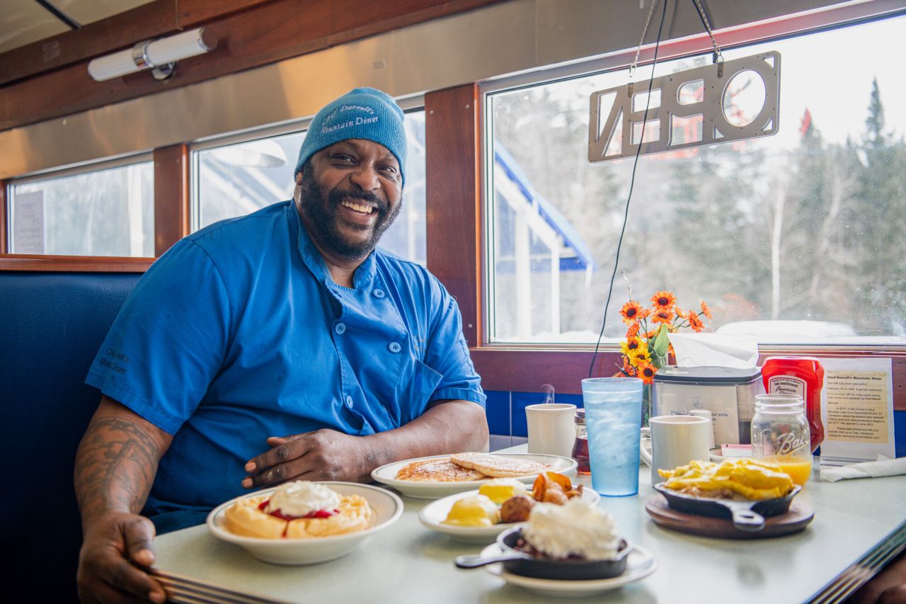 A man poses with a table filled with diner food. 