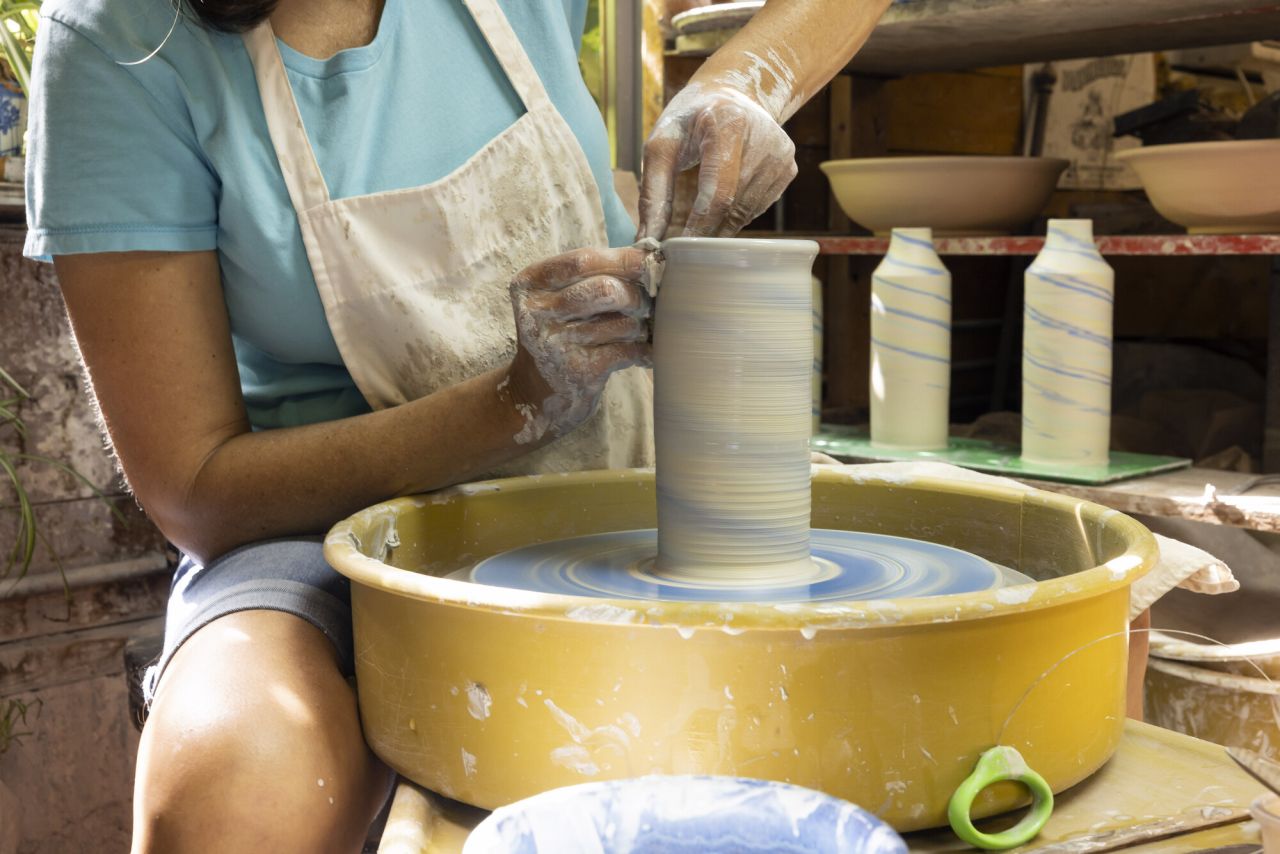 A woman crafts a cylinder out of clay. 