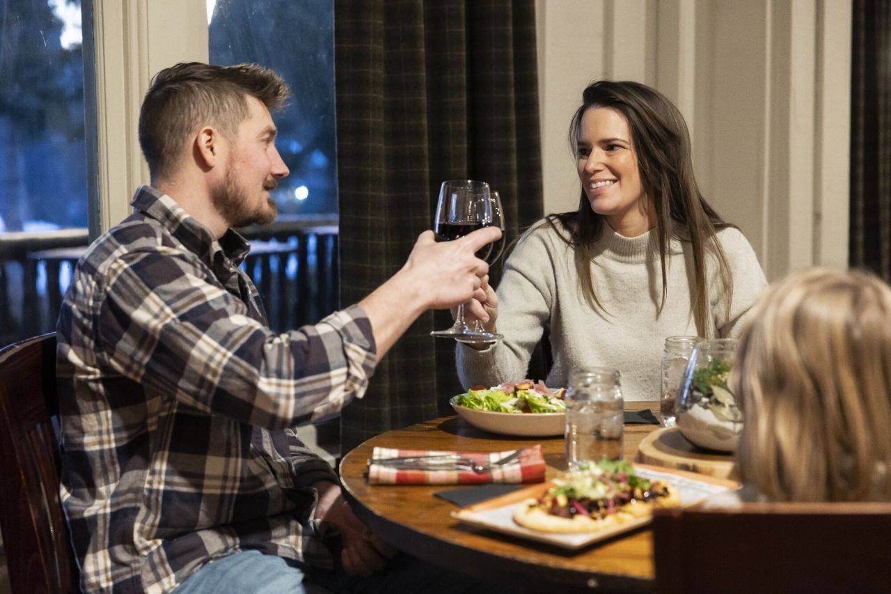 A man and woman cheers wine glasses at dinner.