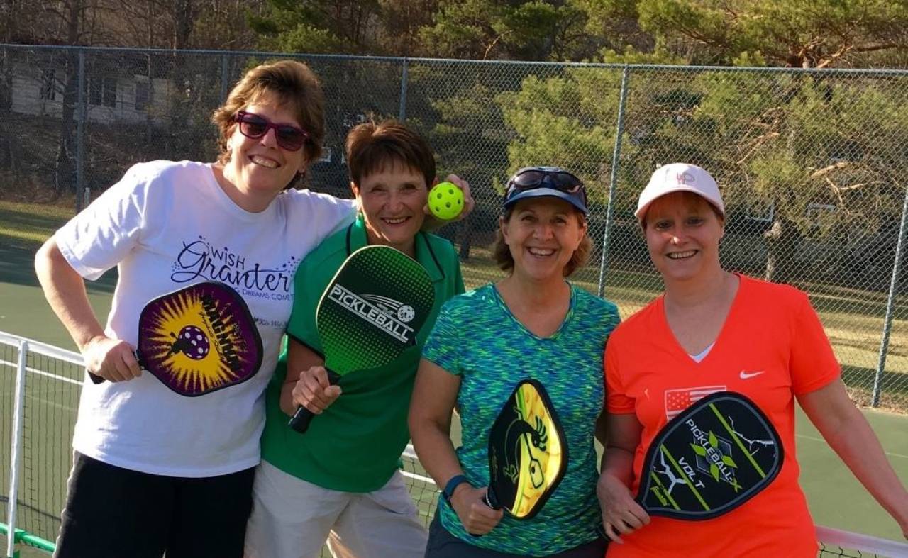 A group of women smile for a picture playing pickleball. 