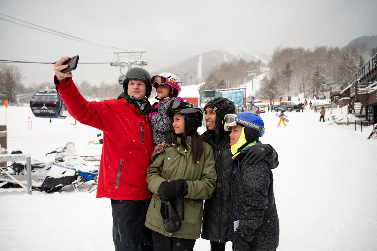 Family of five takes a group selfie at Whiteface Mountain ski resort on snowy day, all dressed in winter and ski gear