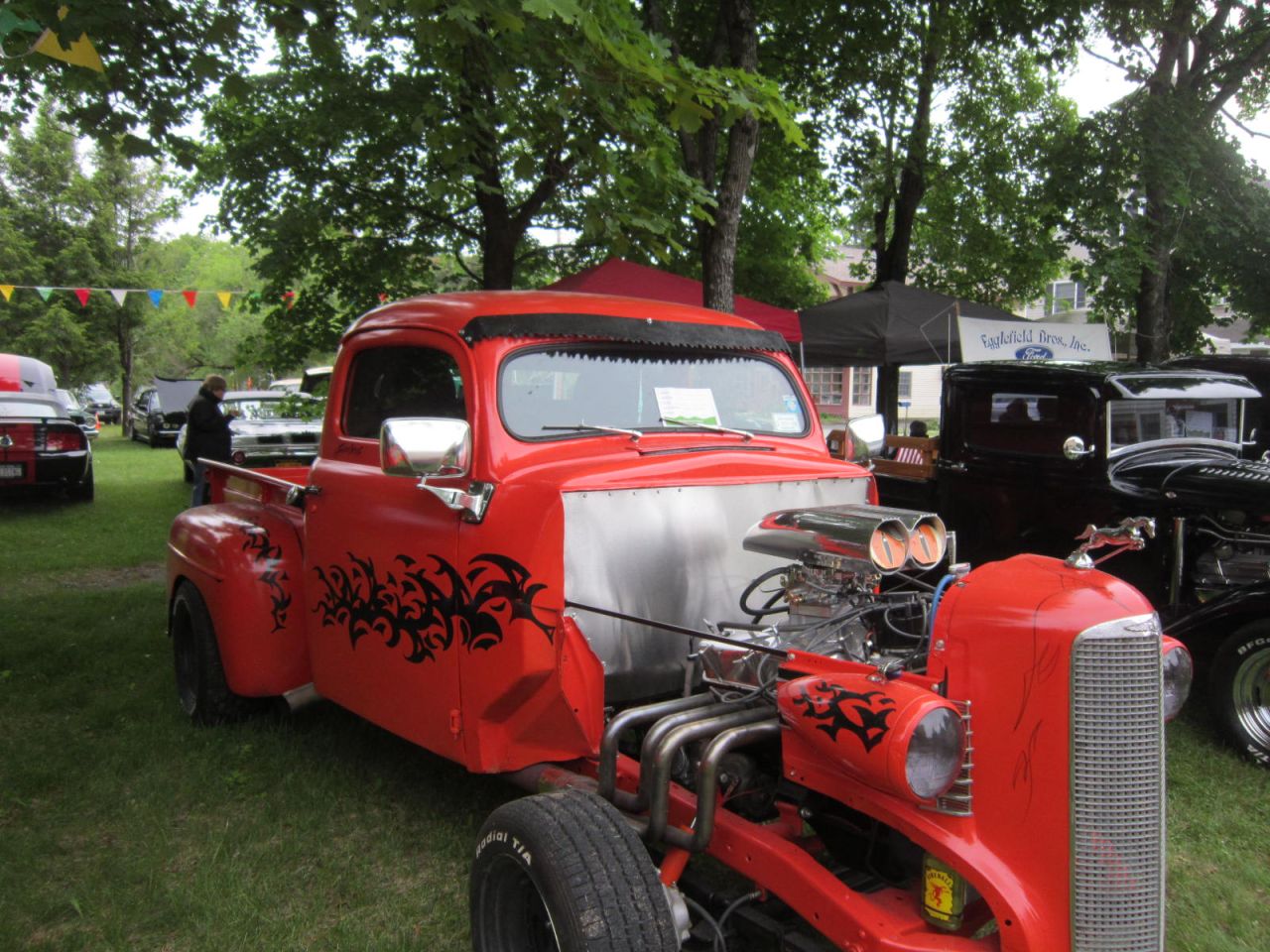 An antique red pickup truck on display at an outdoor car show.