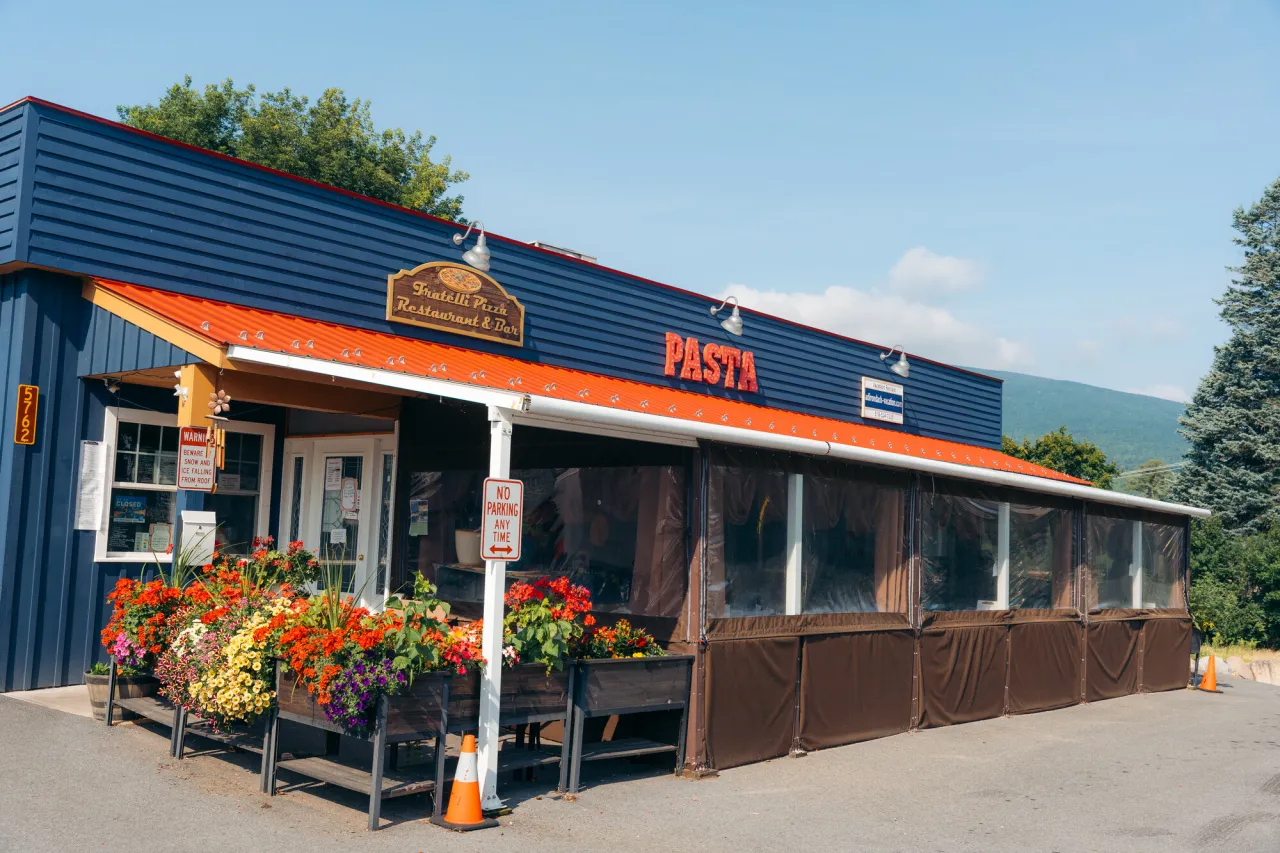 The exterior of a blue, one-story restaurant with front porch and vibrant flower arrangements.