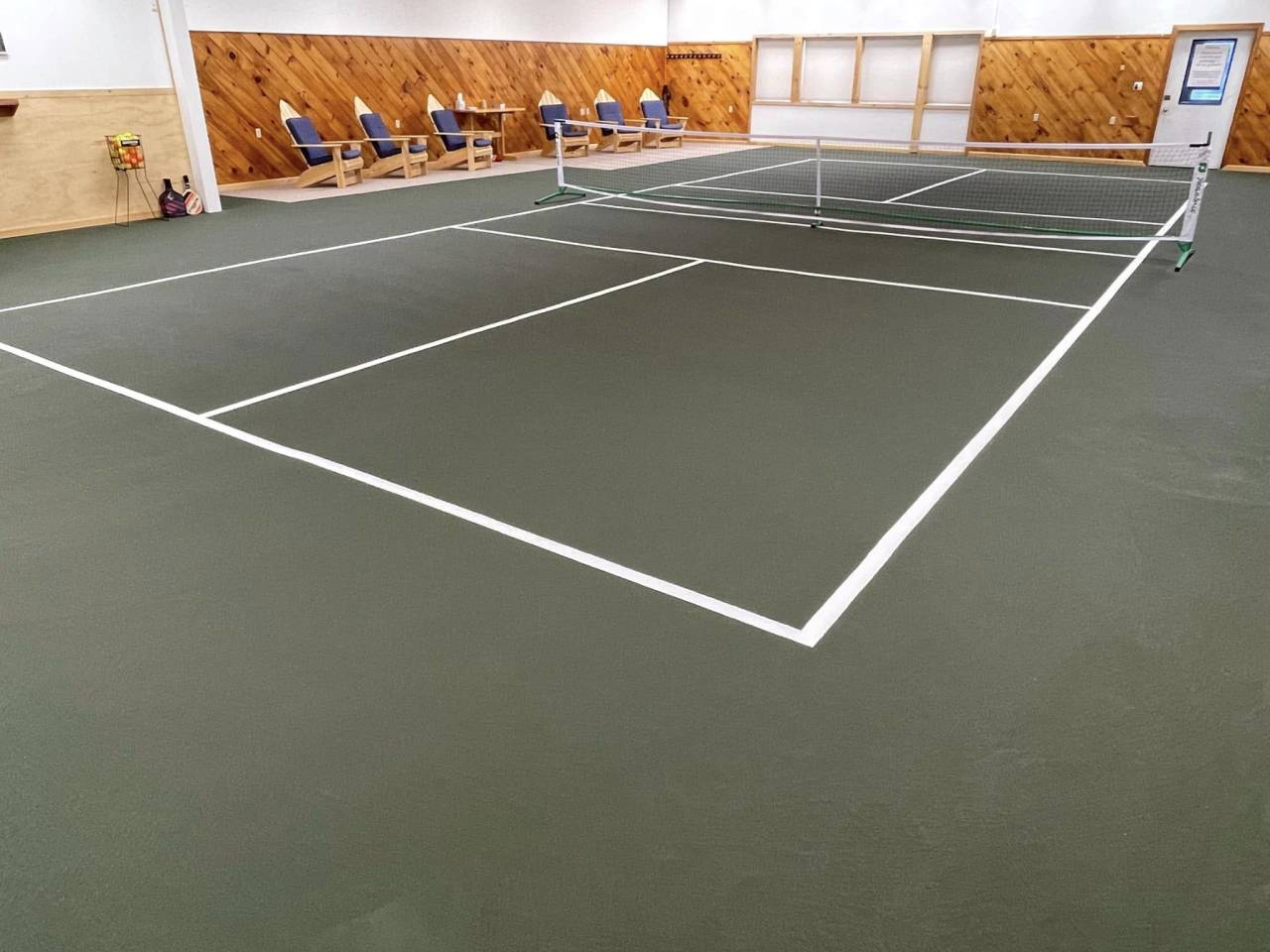 An indoor pickleball court with Adirondack chairs on the sidelines. 