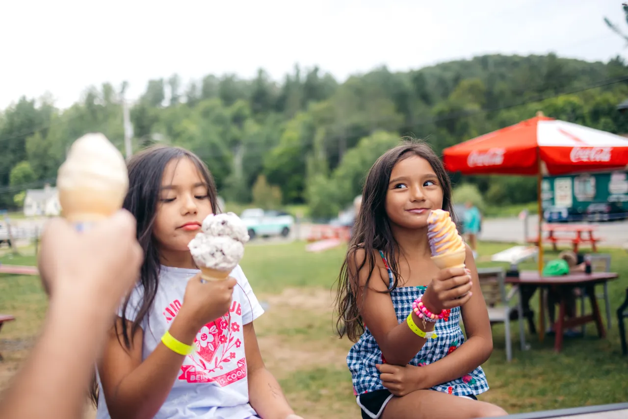 Two young girls eat ice cream at a beach.