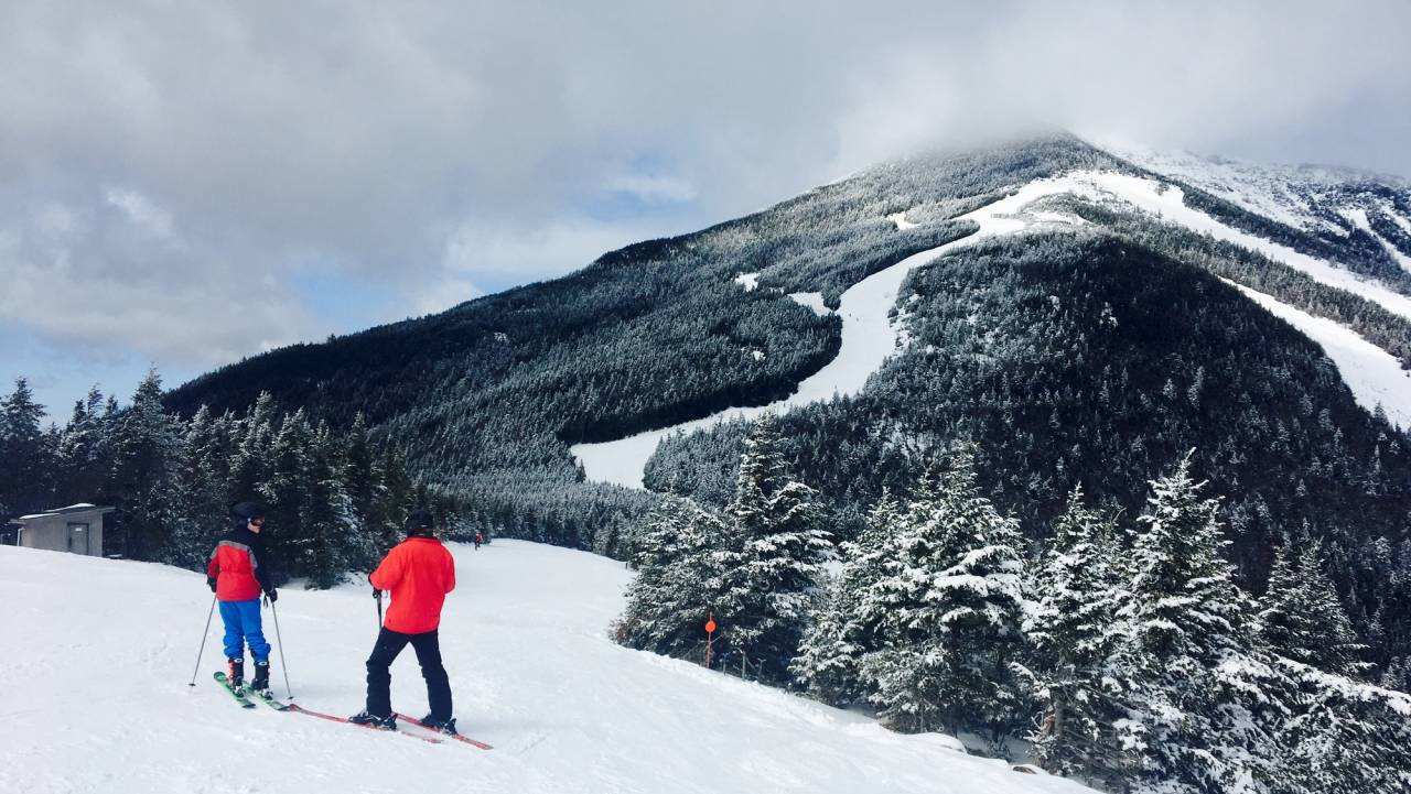 Two skiers at Whiteface Mountain with views of slopes behind them.