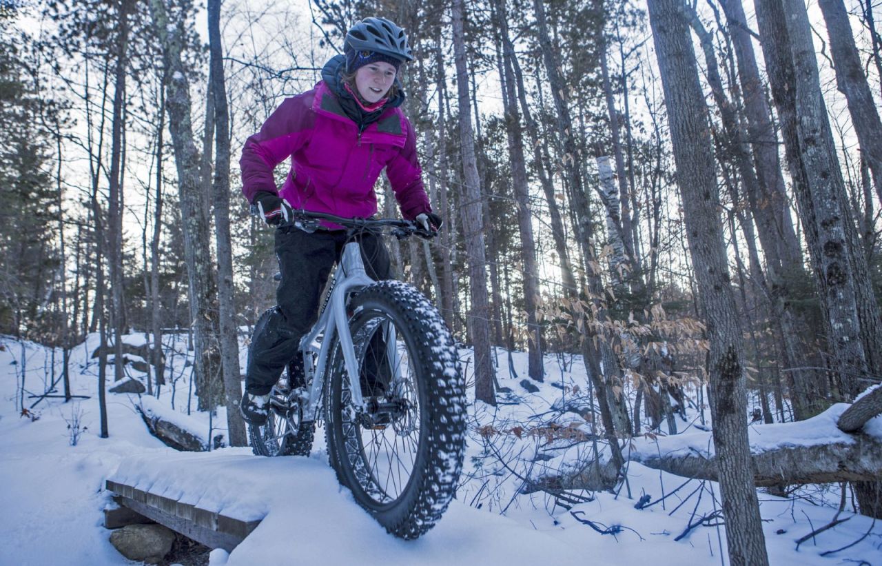 A woman in a pink jacket fat tire bikes in winter.