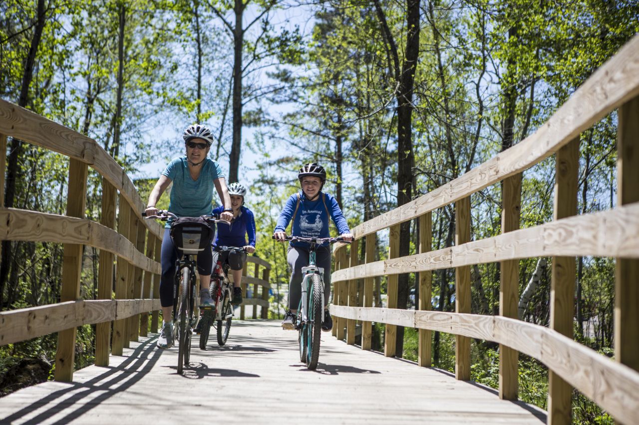A group of cyclists ride along a wooden bridge.  