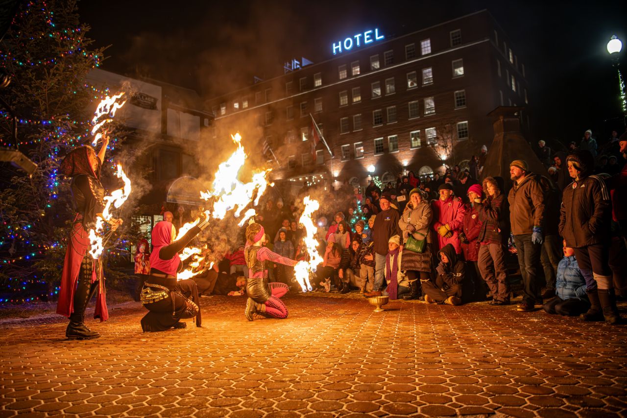 A group of people watch a fire dancing show in the park of a winter town. 