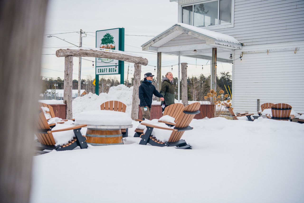A man and woman walk through the snow to get to a restaurant. 