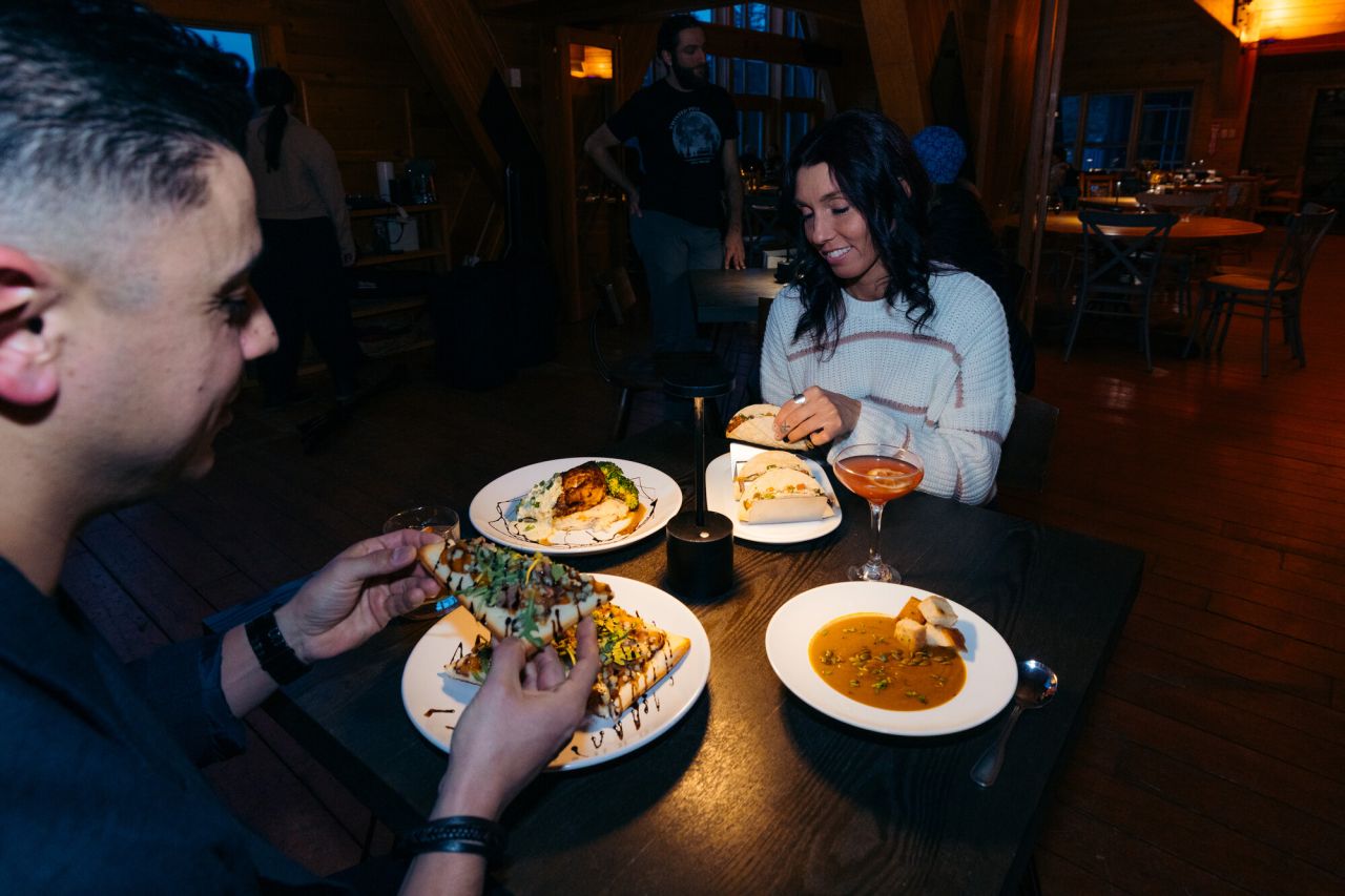 A man and woman dig into an assortment of foods at a low-lit dining room. 
