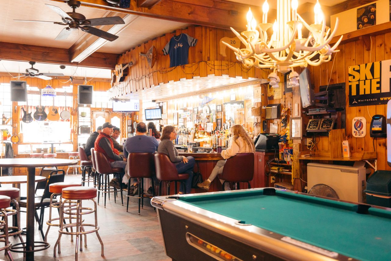 A warm lit bar with a pool table and patrons at the bar. 