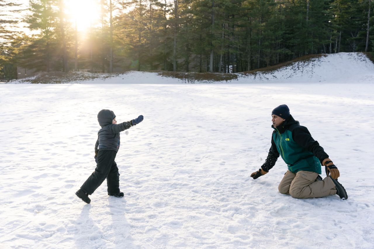 A man plays with his son in the snow in a park.