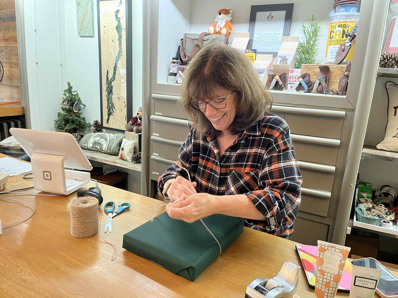 A woman ties a string around a present wrapped in green paper.