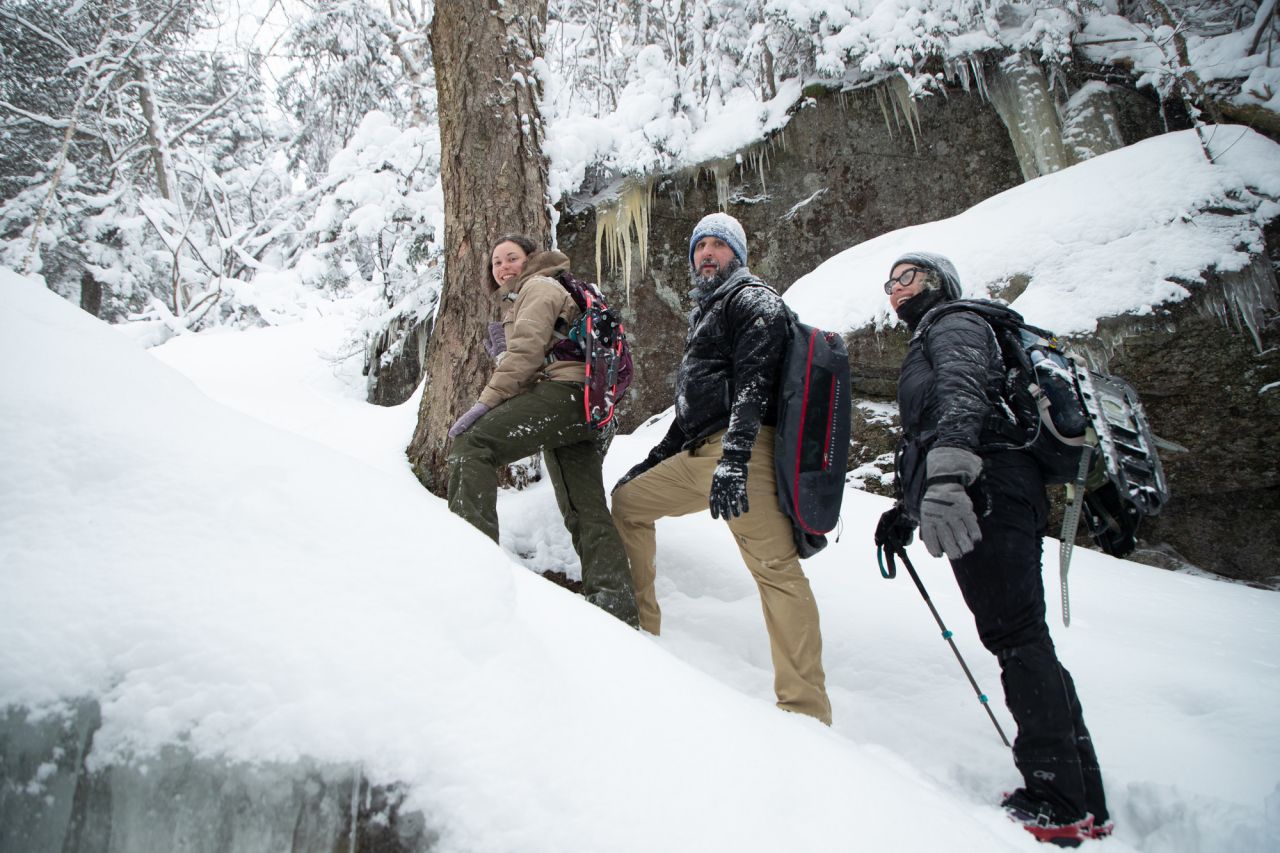 Three people climb up a winter hiking trail covered in ice and snow.