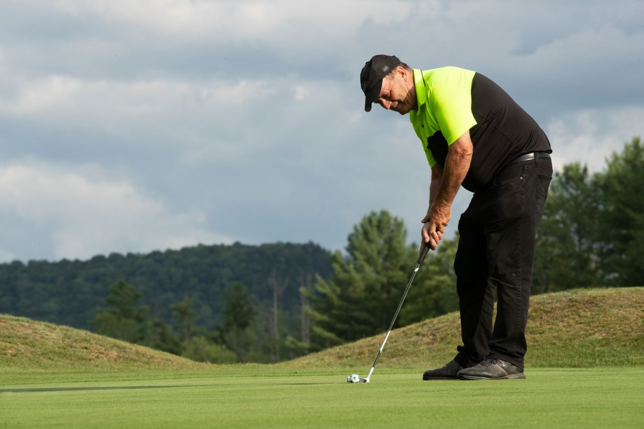 A man sets up a shot while golfing on a green course. 