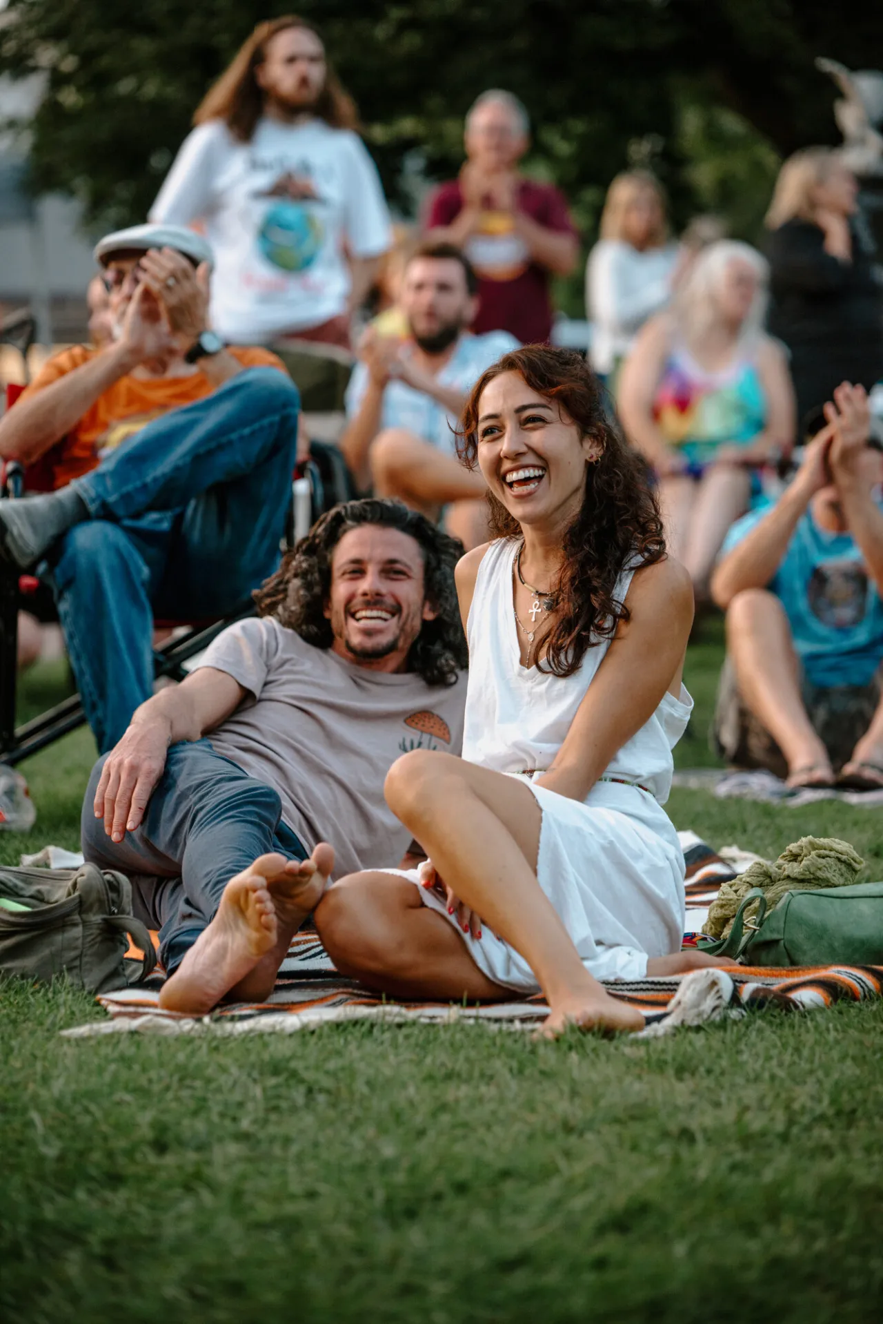 A couple sitting on the grass listening to live music.