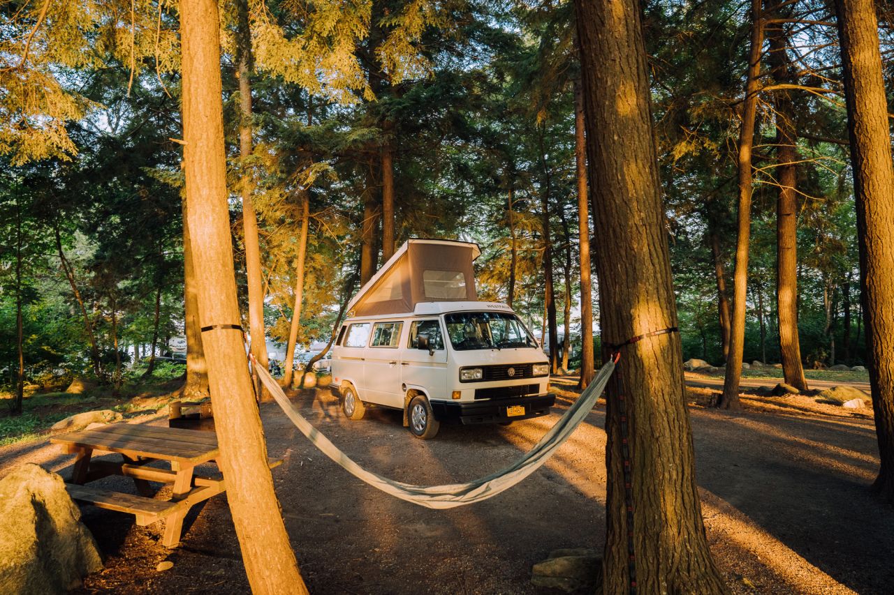 A van sits in between two trees in a camp site with the top hatched popped up at dusk. 