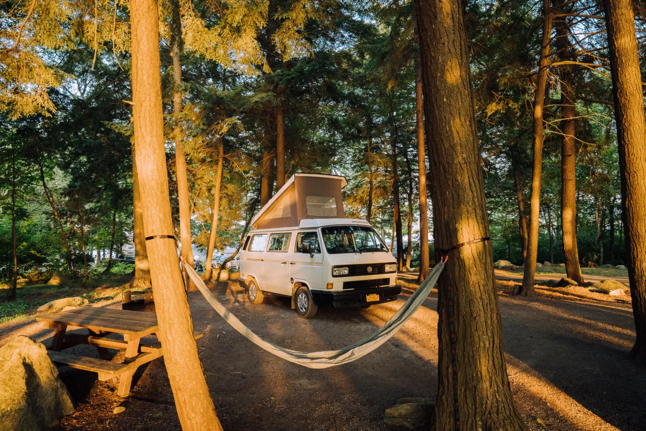 A van parked in a campsite with a hammock in the foreground.