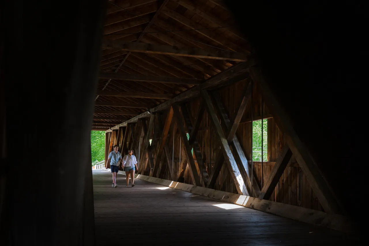 Couple walks along inside of Jay Covered Bridge with sunlight streaming in through windows