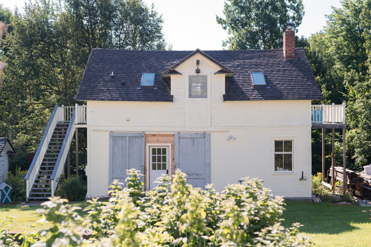 A white barn sits among flowers and greenery. 