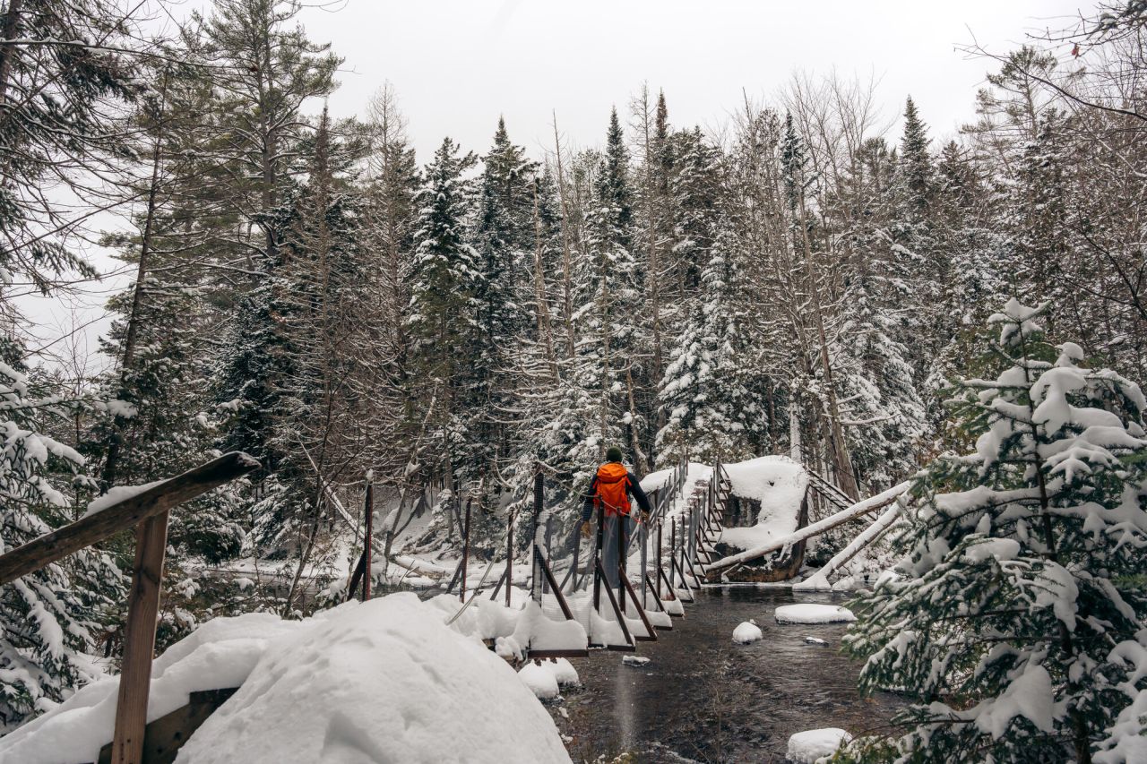 A snowshoer crossing a metal suspension foot bridge