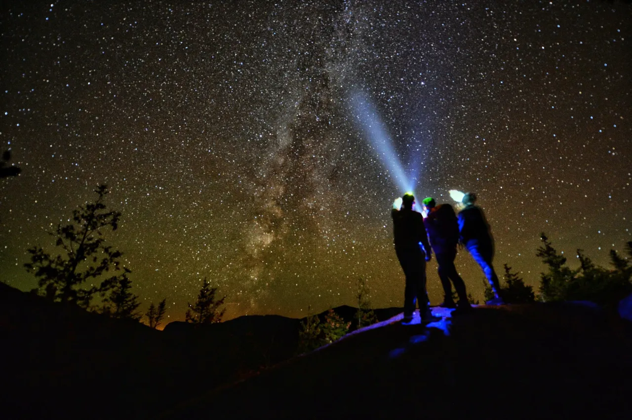 2 people using headlights looking towards a starry sky