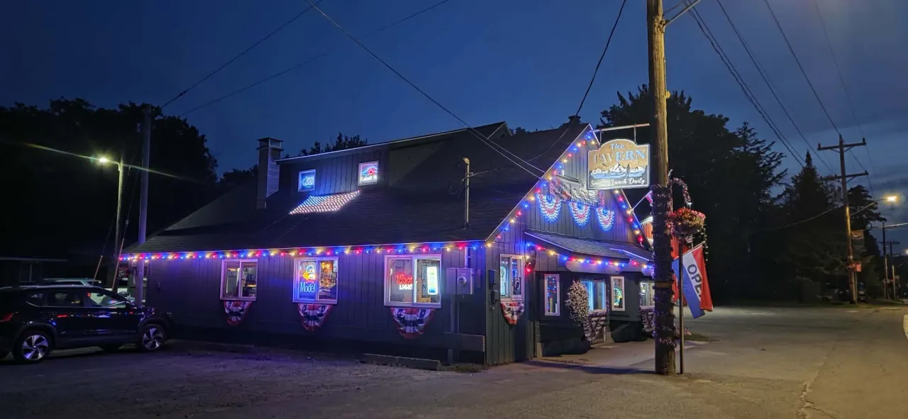 The exterior of a tavern at nighttime, lit with festive holiday lights and American flag bunting.