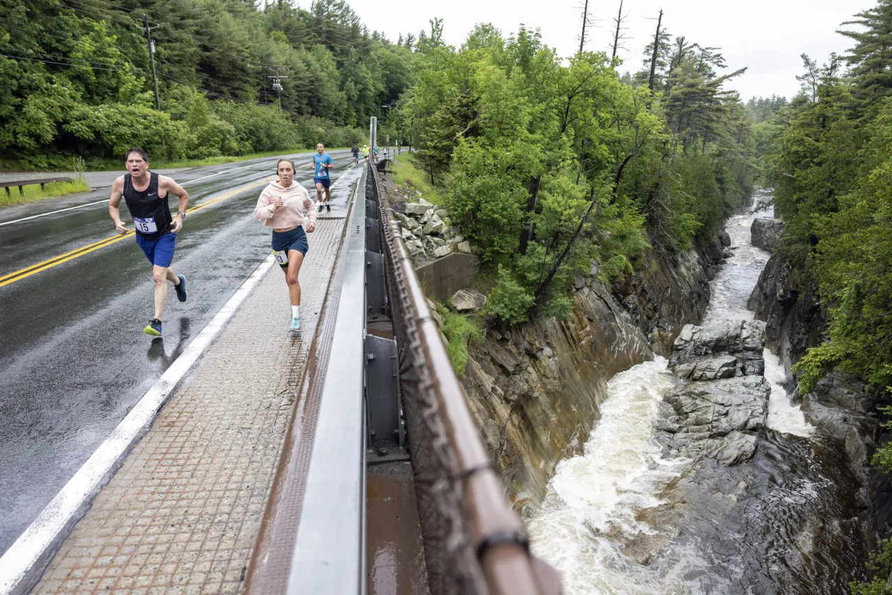 A group of people run on a bridge overlooking rushing waterfalls.