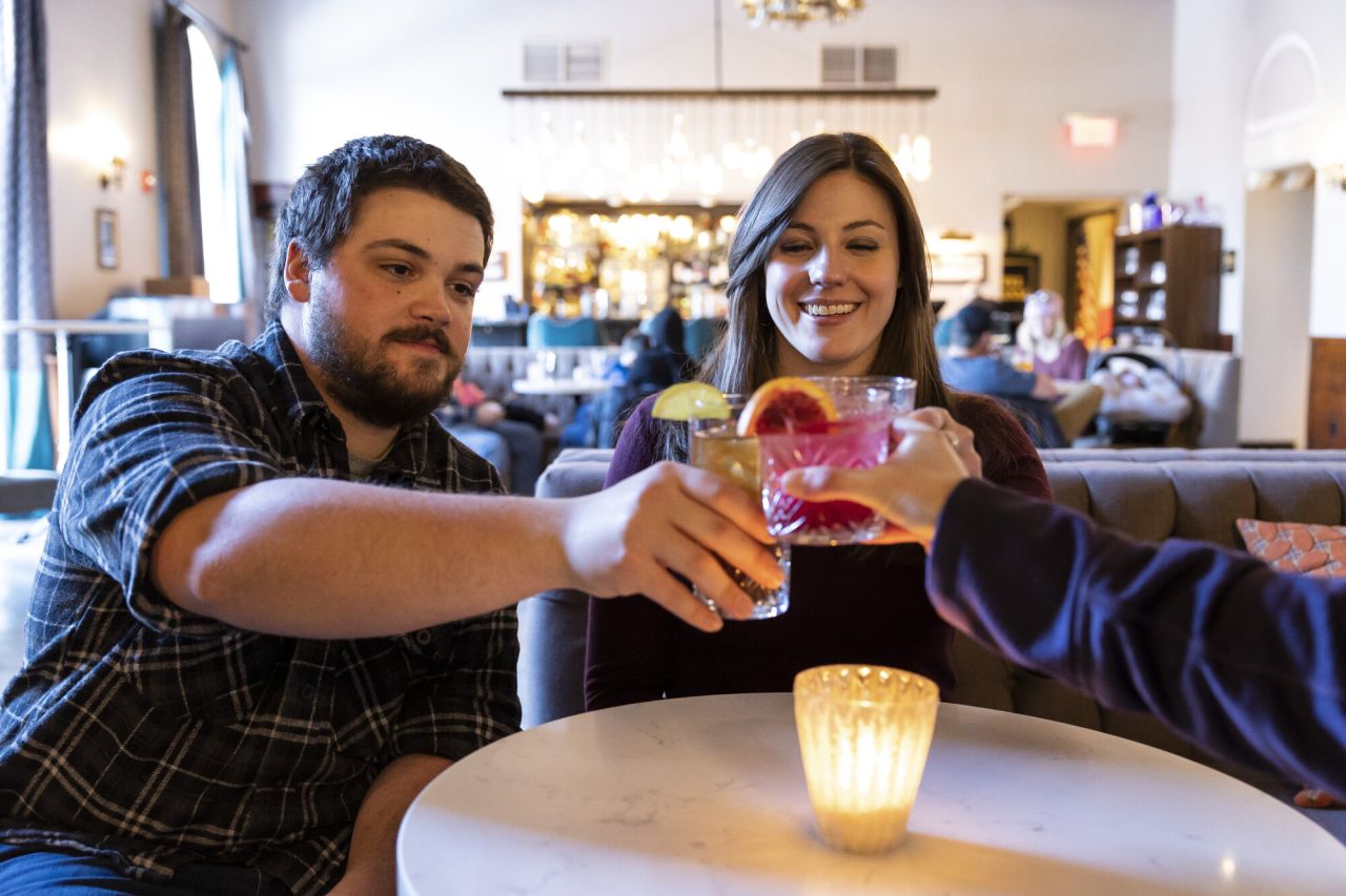 Three friends cheers cocktails together at a brightly lit restaurant.