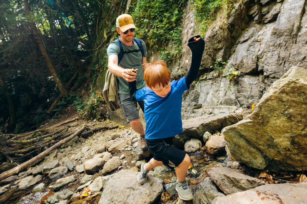 Father holds the hand of a young son walking in front of him on a rocky section of trail