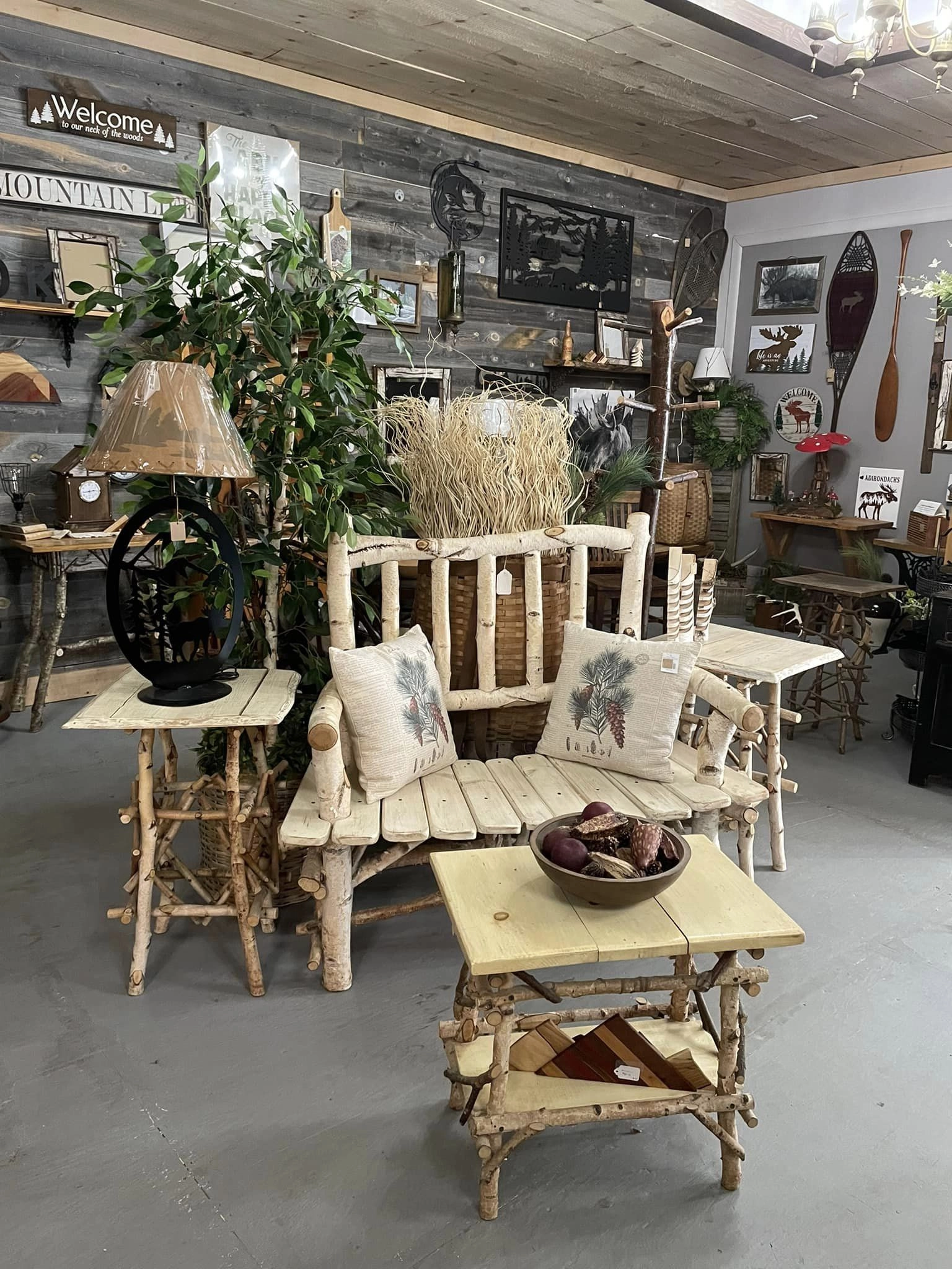 A room full of rustic decor pieces like birch wood bench and matching table and wrought iron lamps and wall hangings