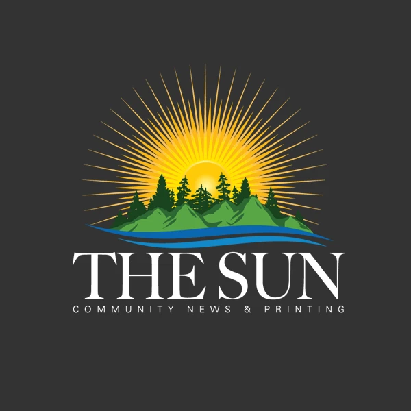 The Sun Logo of a large yellow sun, a body of water, a small green island with tall dark pine trees