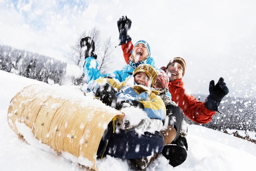 A young family laughs their way down the sledding hill on a tobogan as the snow flies around them